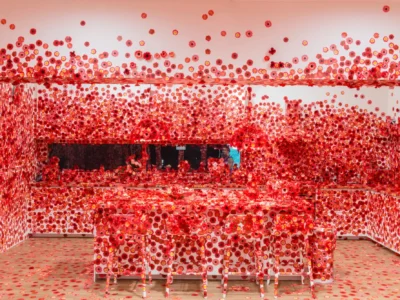 Contemporary art installation by Yayoi Kusama featuring an immersive room covered in thousands of vibrant red floral decals, transforming walls, furniture, ceiling, and decorative objects into a striking polka-dot-inspired environment