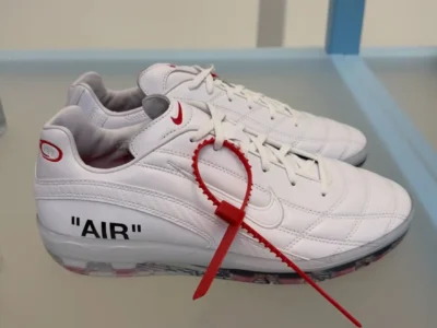 White Virgil Abloh Archive x Nike Cryoshot Tiempo displayed on a showroom table, featuring premium quilted leather, a translucent Cryoshot sole, signature red V.A.A. zip-tie, red mini Swoosh branding, and bold “AIR” typography on the lateral heel