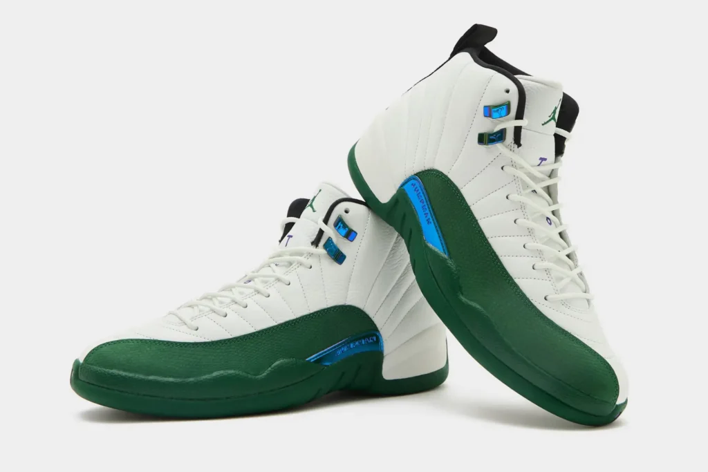 Pair of Air Jordan 12 shoe displayed against a light gray background, featuring white tumbled leather uppers with deep emerald-green mudguards and midsoles. Iridescent blue metallic eyelets and matching side accents add contrast, while black tongue liners and subtle purple detailing complete the classic basketball silhouette