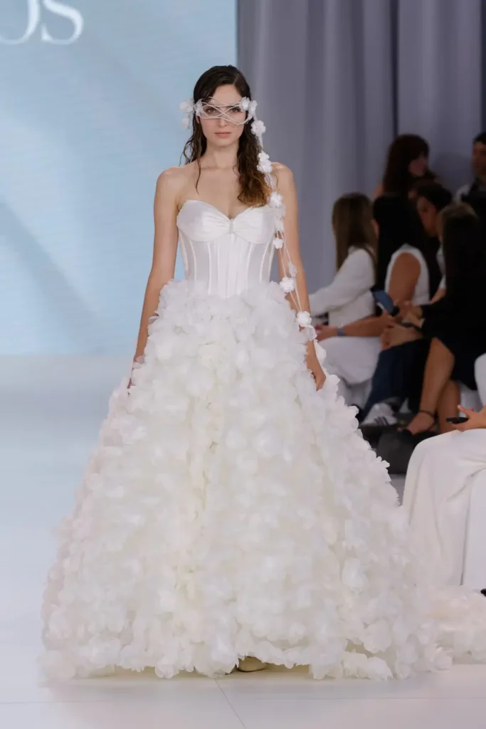 Romantic floral wedding gown with corseted bodice, oversized three-dimensional flower appliqués, and matching floral face adornment