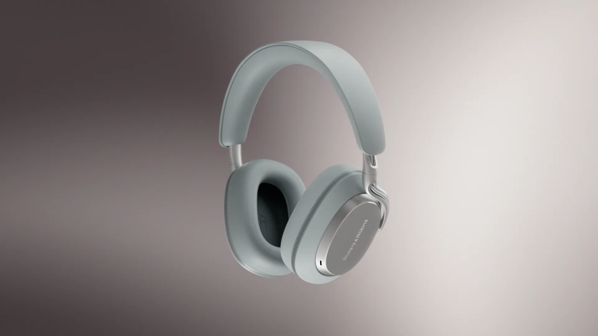 Bowers & Wilkins over-ear wireless headphones in a light mist-gray finish, suspended against a neutral gradient backdrop, showcasing the sleek silhouette and premium material