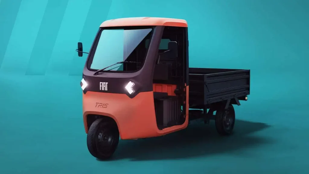 Compact orange Fiat Professional Tris electric three-wheeled pickup truck displayed against a blue studio backdrop. The utility vehicle features a single-cab layout, open cargo bed, and minimalist commercial-focused design