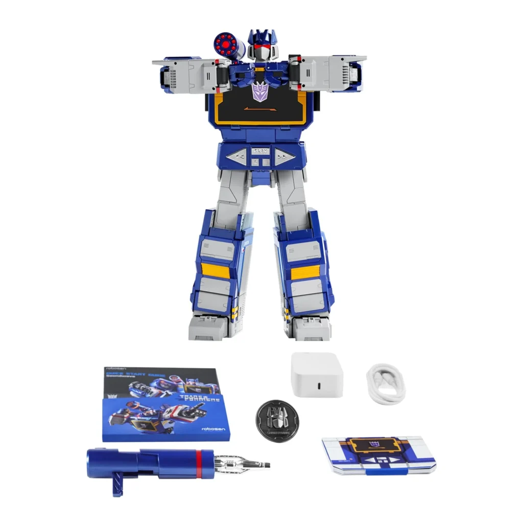 Soundwave robot displayed with included accessories, featuring the shoulder cannon attachment, collector coin, documentation, charging adapter, cable, and display component