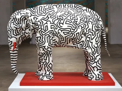Keith Haring-inspired elephant sculpture covered in bold black-and-white graphic linework, displayed on a red pedestal inside a contemporary gallery space