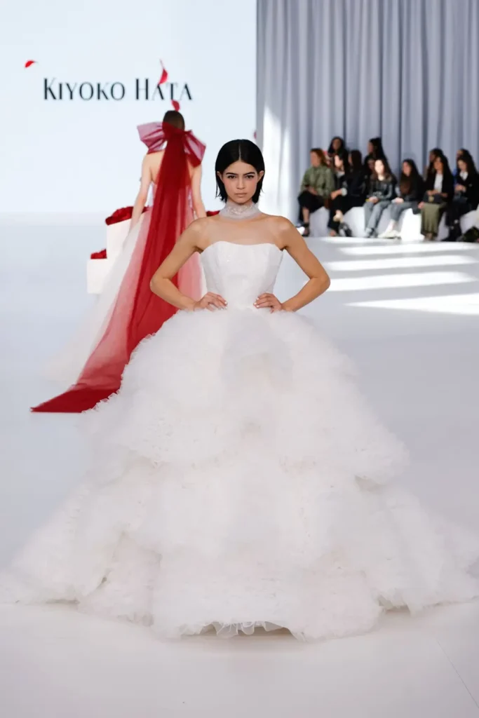 Strapless bridal ball gown with sparkling bodice, layered textured skirt, and elegant choker presented on the runway