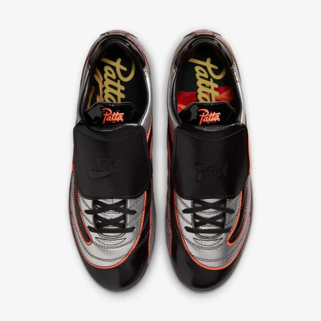 Top-down view of the shoe pair displaying black lace covers embossed with Nike and Patta logos, metallic silver toe boxes, and custom graphic insoles peeking through the opening