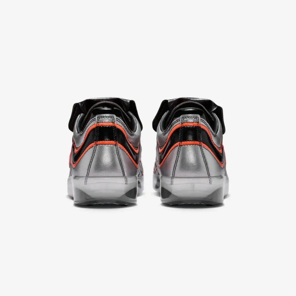 Rear view of the shoe highlighting metallic silver heel panels, black patent overlays with orange-red detailing, central pull tabs, and frosted translucent heel tool