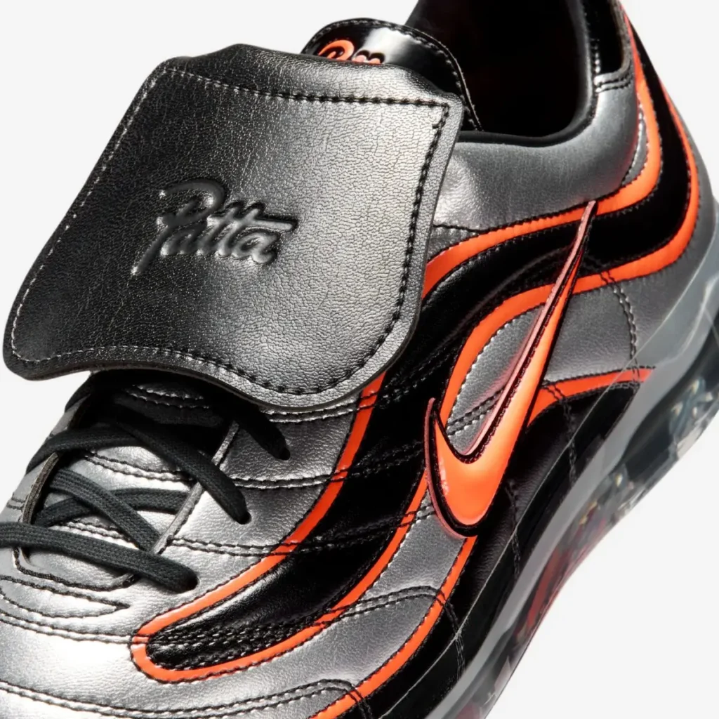 Close-up of the removable black leather tongue flap embossed with Patta branding, paired with a bright orange Swoosh and layered metallic silver and black upper construction