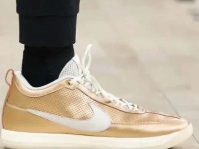 Close-up side profile of Devin Vassell’s metallic gold Nike BOOK 2 Player Exclusive sneaker featuring a shimmering perforated upper, white Swoosh branding, and a clean white sole during NBA Finals preparation