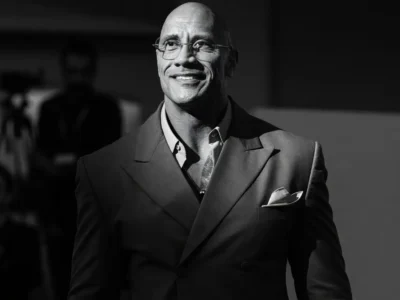 Dwayne Johnson in a tailored gray suit and glasses, smiling confidently — black and white editorial portrait for his 2026 career evolve