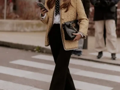 Street style look featuring a gold textured jacket, white button-down shirt with polka-dot tie, black tailored trousers, oversized designer sunglasses, and vibrant pink embellished flats while crossing a city street