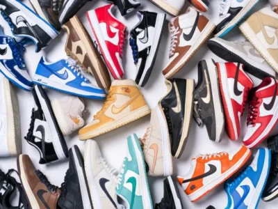 A large collection of Nike low-top and mid-top sneakers arranged in a flat-lay display, showcasing a variety of colorways, materials, and classic silhouettes. The assortment features patent leather, smooth leather, and canvas designs in vibrant shades of red, blue, orange, black, cream, brown, and mint, highlighting the diversity and enduring appeal of Nike’s iconic lifestyle footwear lineup