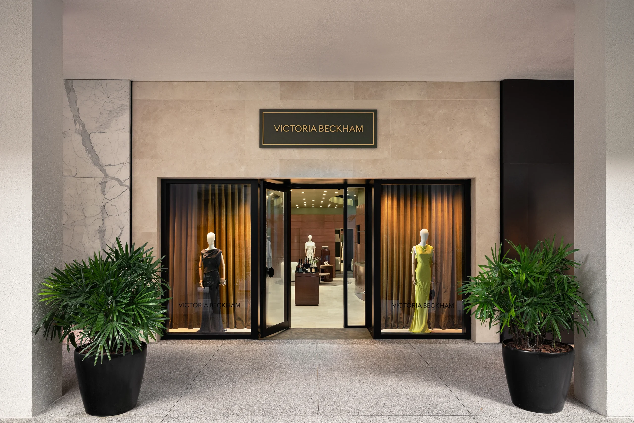 Victoria Beckham’s first U.S. store entrance at Bal Harbour Shops, Miami. Elegant minimalist storefront with black-framed windows, potted palms, and mannequins showcasing ready-to-wear looks. Open through September 2026