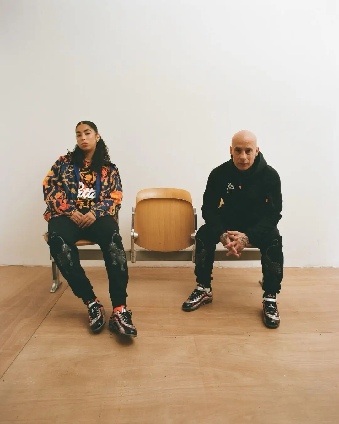Campaign image featuring two models seated beside an empty chair, dressed in Patta apparel and wearing the Patta x Nike Cryoshot Mercurial R9, highlighting the collection’s connection to football culture and contemporary streetwear