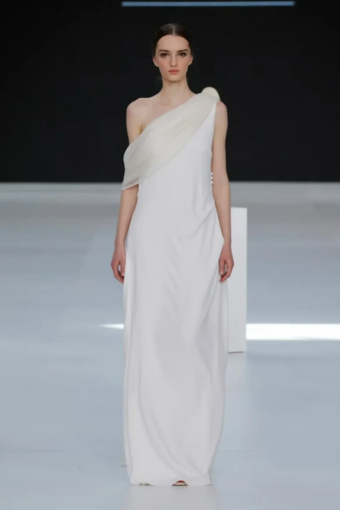 Minimalist one-shoulder wedding gown with soft draping, Grecian-inspired silhouette, and floor-length flowing skirt