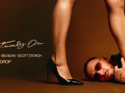 Promotional cover art for “Body Drop” by HUGEL, Big Sean, and Scott Storch. A man wearing tinted sunglasses and a green blazer lies on a brown studio floor while a woman in glossy black stiletto heels stands over him. The minimalist composition uses warm brown tones and dramatic fashion-inspired styling, with the song title and artist names displayed on the left side