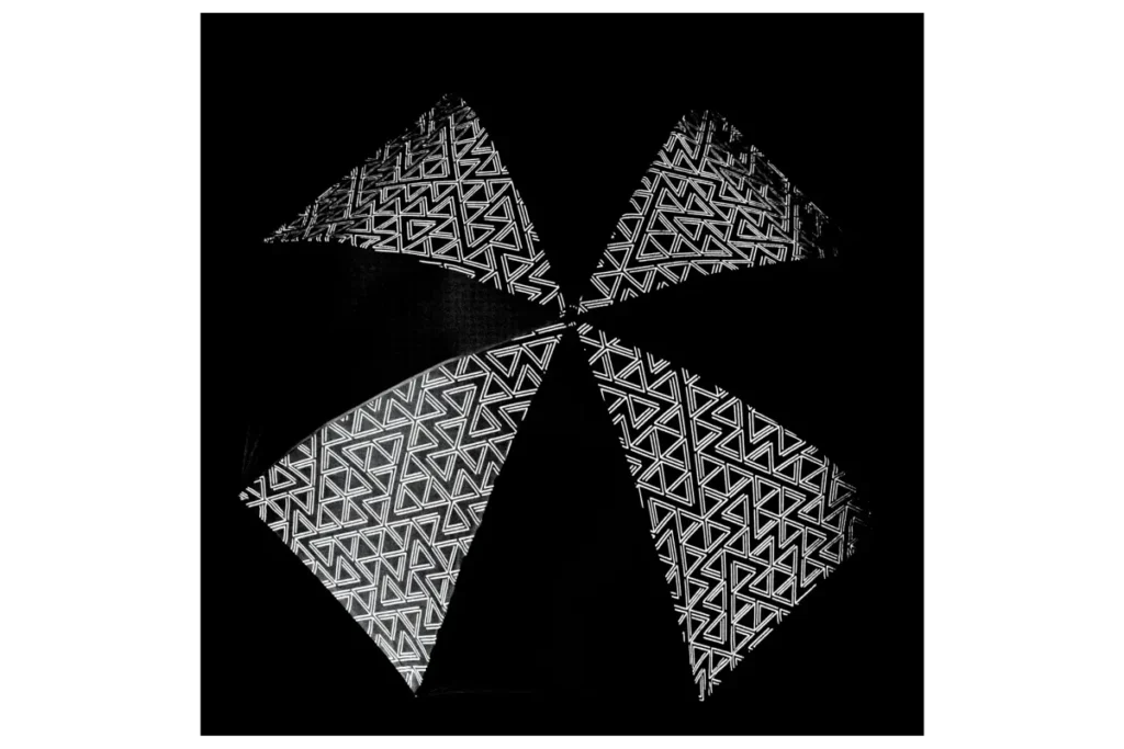 Reflective geometric-pattern umbrella canopy photographed in darkness, showcasing highly visible white triangular graphics that illuminate dramatically against a black background