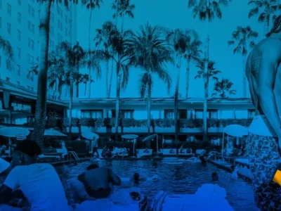 A blue-toned photograph captures a lively poolside scene framed by tall palm trees and a historic hotel backdrop. Guests gather around the water, lounging and socializing beneath the warm outdoor setting. In the foreground, a shirtless figure with braided hair walks along the pool deck wearing patterned shorts, holding a brightly illuminated object that contrasts against the monochromatic blue treatment. The image blends leisure, nightlife, and contemporary lifestyle aesthetics with a cinematic, editorial feel