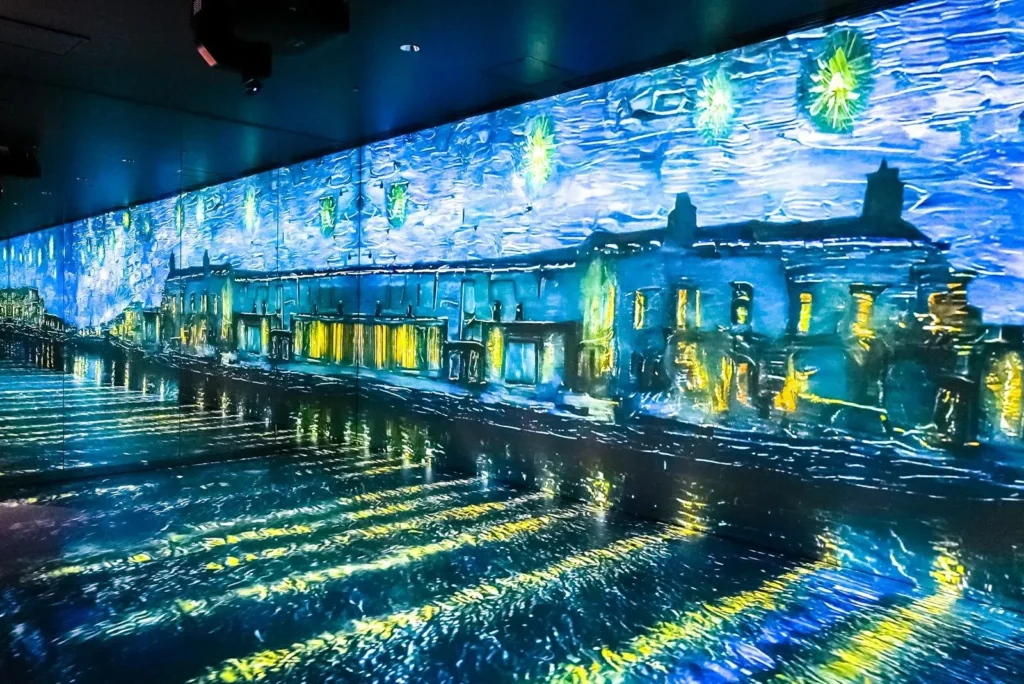 A panoramic projection of a glowing waterfront cityscape inspired by impressionist art covers the walls and floor of an immersive exhibition space