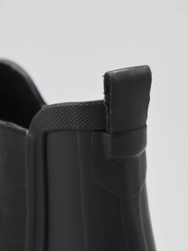 Detailed close-up of the rear pull tab attached to the boot’s heel. The textured collar and molded rubber construction showcase practical design elements for easy on-and-off wear