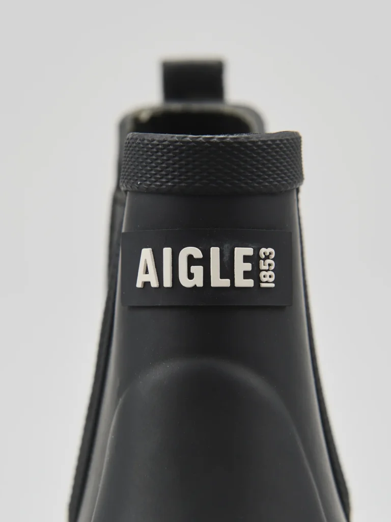 Front-facing close-up of the boot’s upper shaft featuring the embossed “AIGLE 1853” branding. The textured collar and smooth matte-rubber finish stand out against the minimalist studio background