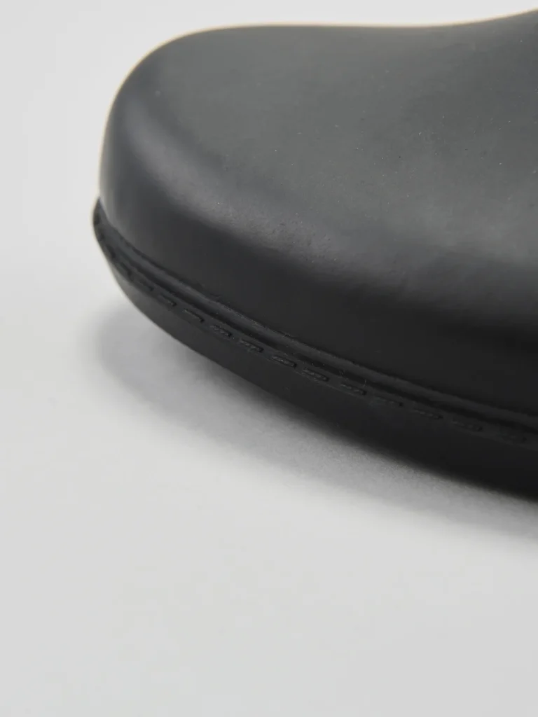 Macro detail of the rounded toe box and lower edge of the matte-black rubber boot. Fine stitching and the smooth waterproof finish are highlighted in the close-up product shot