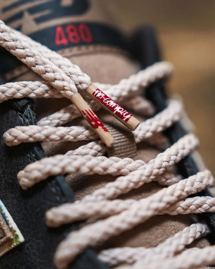 Detailed shot of the cream-colored rope laces on the New Balance Numeric 480 shows co-branded lace tips featuring No-Comply and New Balance logos, with the red “480” tongue marking view in the background