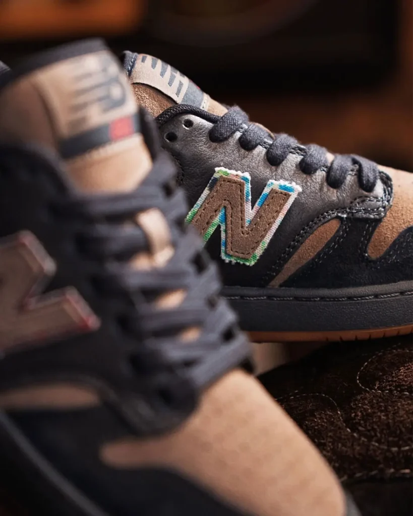 Close-up of the medial side of the collection shoe reveals a contrasting embroidered “N” logo outlined in blue and green tones against black leather and tan suede overlay