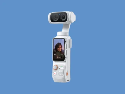 White edition Insta360 handheld camera shown at an angle against a soft blue background, showcasing its dual-lens camera module, touchscreen interface, and streamlined portable form factor
