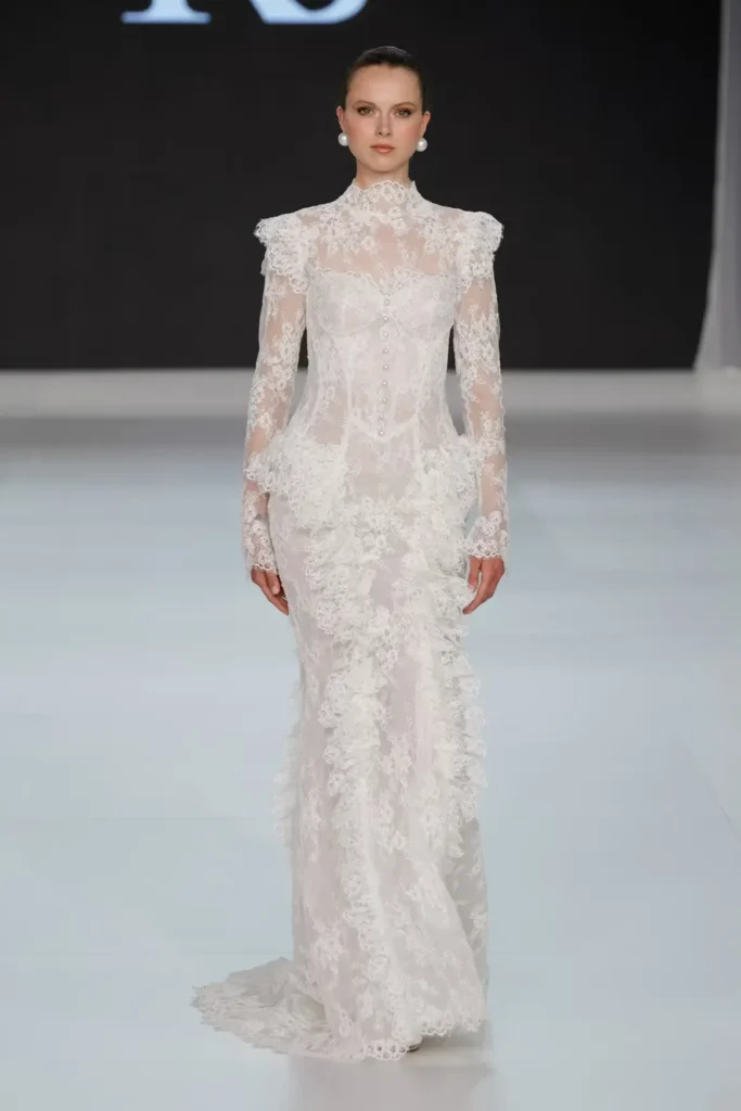 Vintage-inspired lace wedding gown with high neck, sheer sleeves, pearl-button bodice, and intricate embroidered detail