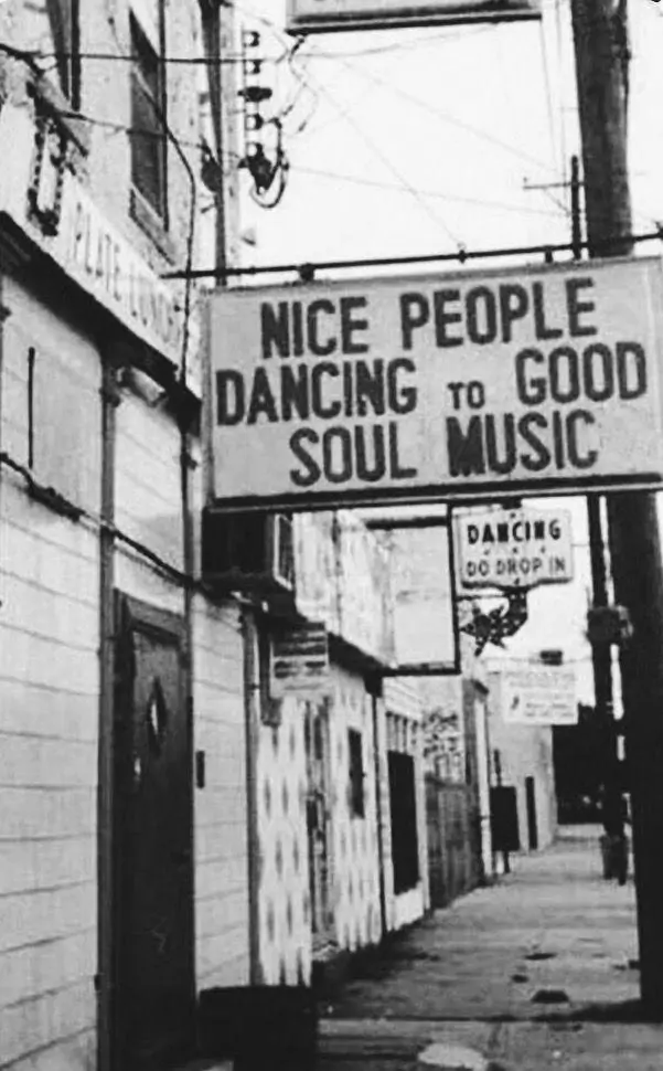 Grainy black-and-white street photograph featuring a vintage marquee sign reading “Nice People Dancing to Good Soul Music” above a quiet urban sidewalk