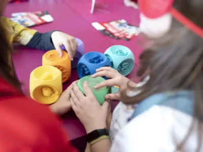 Children interact with colorful tactile educational game pieces during a hands-on design workshop, exploring shapes, textures, and sensory learning through collaborative play as part of an inclusive educational experience
