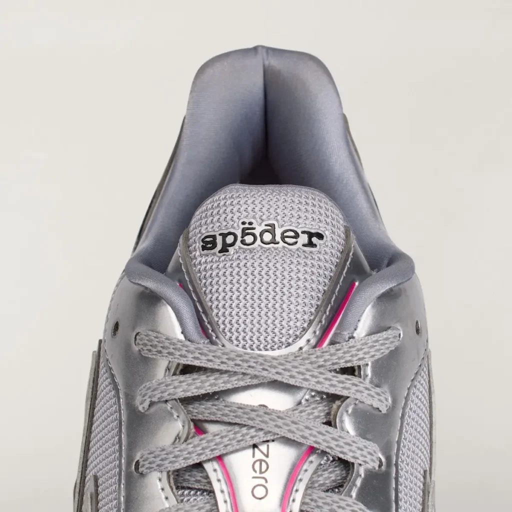 Close-up of the tongue and collar highlighting the embroidered Sp5der logo, grey mesh tongue construction, metallic eyelets, grey laces, and pink trim framing the central lace panel