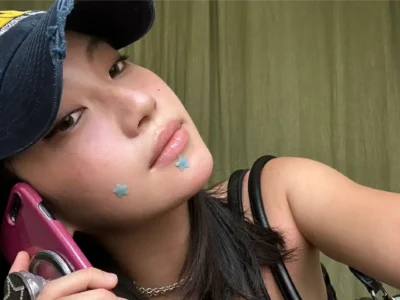 A fresh-faced moment in street style: blue distressed cap tilted just right, baby-blue star stickers glowing on dewy skin, and that effortless mirror selfie vibe. Casual cool with a playful edge—perfect for summer days and city nights.