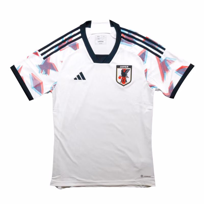 Front view of the adidas Japan Football Association white away jersey featuring a clean white body, geometric red and blue sleeve graphics, black Three Stripes on the shoulders, black V-neck collar, adidas logo, and the official JFA crest.