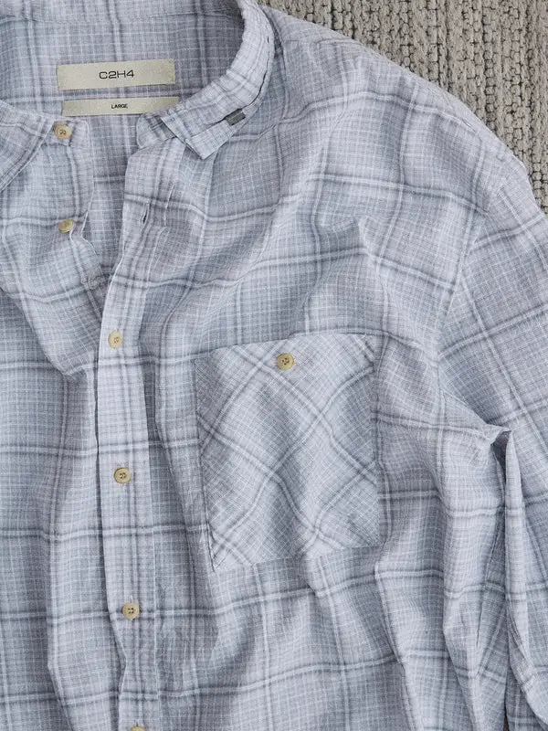 Close-up of a light blue plaid button-up shirt with a soft textured fabric, featuring a band collar, natural buttons, and a single chest pocket with a buttoned flap.