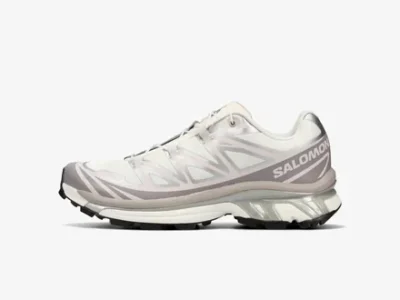 Side profile of the Salomon XT-6 shoe in a white, silver, and soft taupe colorway. The shoe features a lightweight mesh upper with glossy synthetic overlays, Quicklace fastening system, reflective detailing, Salomon branding across the heel, and a sculpted cushioned midsole above a black trail outsole