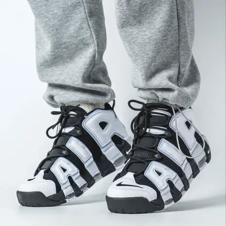 On-foot view of the Nike Air More Uptempo 'Cobalt Bliss' sneakers paired with gray sweatpants, showcasing the bold white AIR lettering, black nubuck upper, and subtle icy blue accents.