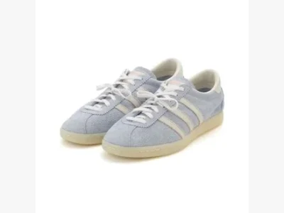 Three-quarter product view of light blue suede adidas low top shoe featuring white leather stripes, white laces, and translucent gum soles against a white studio backdrop
