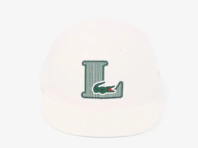 White snapback cap featuring a green striped varsity-style "L" logo with the signature Lacoste crocodile embroidered across the base, shown against a clean white background