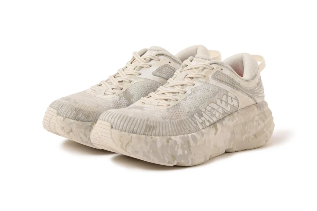 Angled view of the off-white HOKA Project Transport featuring tonal camouflage graphics, oversized HOKA branding, breathable mesh construction, and a matching camouflage foam midsole