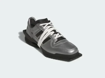 Three-quarter front view of the silver adidas sneaker emphasizing the metallic leather upper, bold white wraparound laces, black Three Stripes, extended forefoot platform, and futuristic design lang