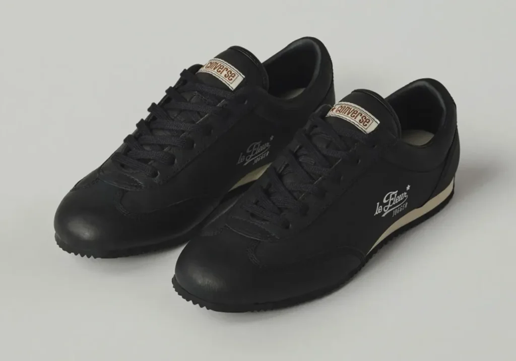 Black leather Converse le FLEUR* Jogger displayed from a front three-quarter angle with tonal black upper, slim retro runner sil, and white side brand