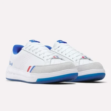 Front three-quarter pair view of white leather sneakers with blue collar, grey suede overlays, red/blue racing stripes, translucent blue sole.