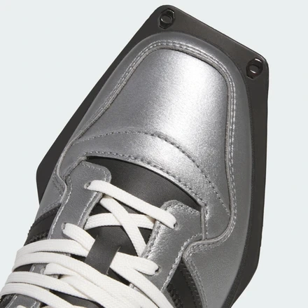 Close-up of the adidas Forum SQ showcasing a metallic silver leather toe box, oversized white laces, and the extended square black outsole plate with exposed hardware against a light gray background.