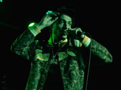 Casper TNG olding a wired microphone mid-song on a dimly lit stage under vivid green concert light
