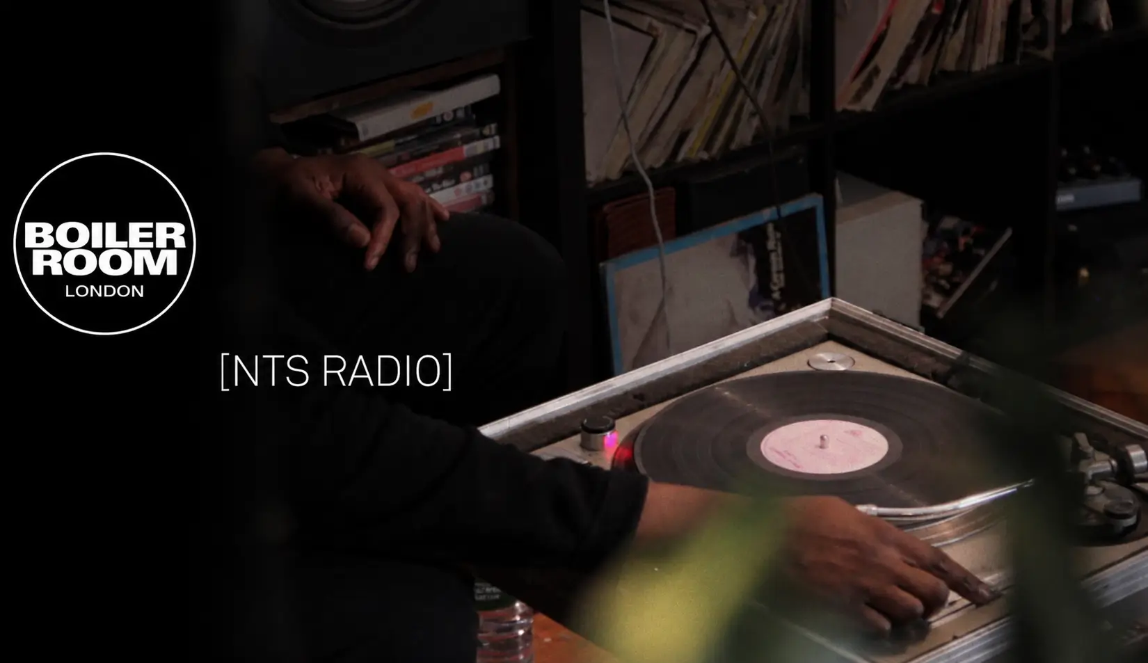 Boiler Room London logo displayed beside a turntable spinning a vinyl record, with an NTS Radio label over a cozy record-filled listening room.