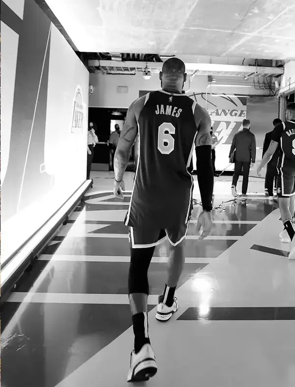 Black-and-white photo of LeBron James walking through the arena tunnel wearing his Los Angeles Lakers No. 6 jersey before or after a game.