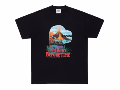 Black short-sleeve Tee with a colorful The Land Before Time graphic showing dinosaurs crossing a prehistoric landscape beneath an erupting volcano, finished with the film title in bold red letter