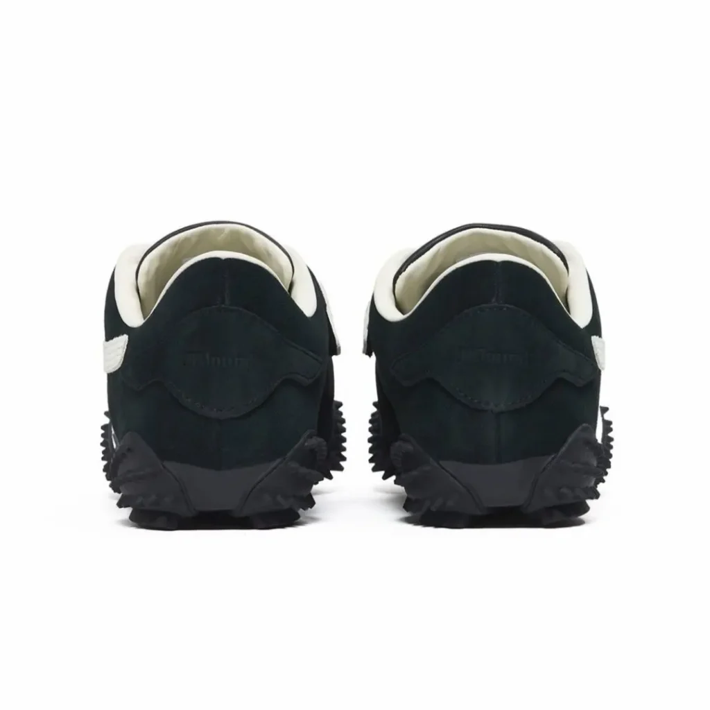 Rear view of black suede Puma x JJJJound shoe with embossed “JJJJound” on the heels, white heel collars, and black studded rubber outsole
